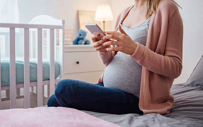 Pregnant woman sitting on her bed looking at her phone