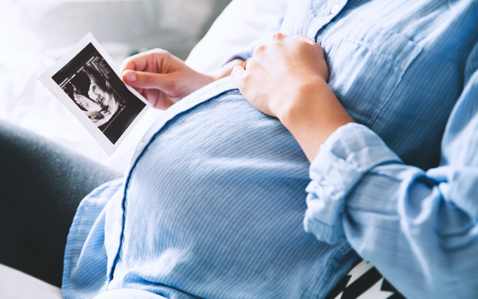 Pregnant woman holding an ultrasound whilst cradling her belly