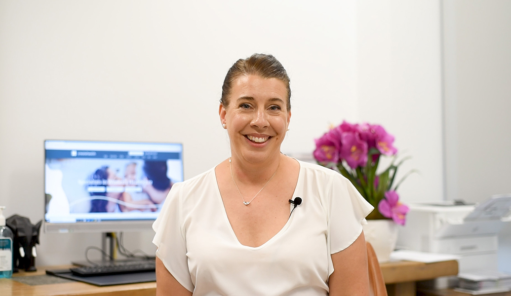 Woman smiling at the camera with Create Health website displaying on a computer in the background