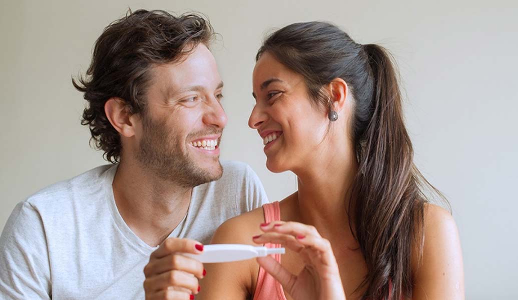 Happy couple smiling at each other while holding a pregnancy test