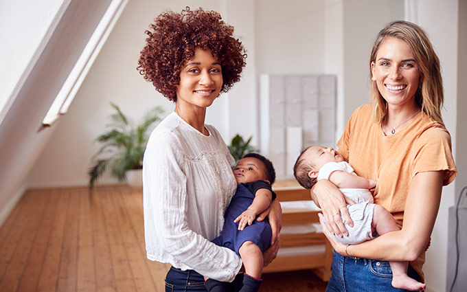 Two women holding their babies and smiling at the camera