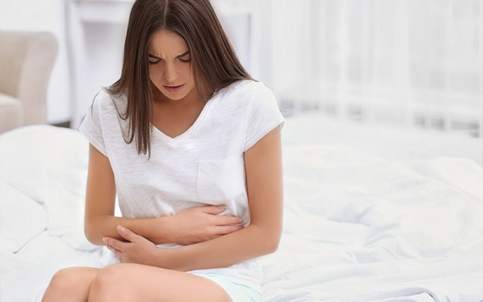 Woman sitting in bed clutching her abdomen in pain