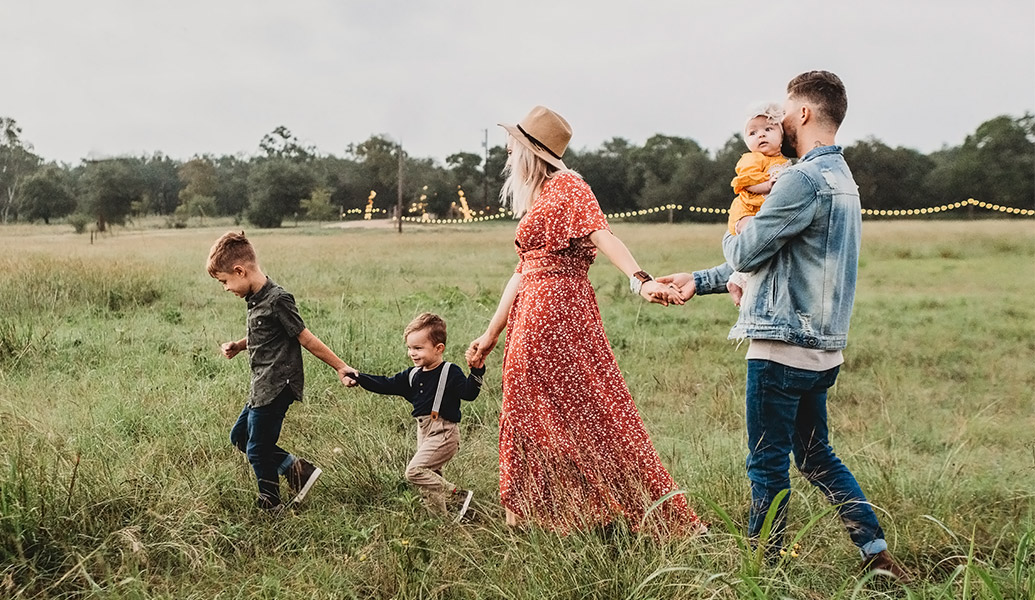 Young family with 3 small children walking through a field