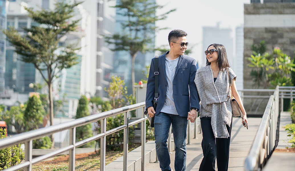 Asian couple smiling at each other, walking whilst holding hands