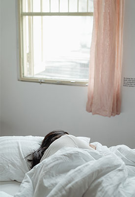Woman lying in bed in a white room with a pink curtain