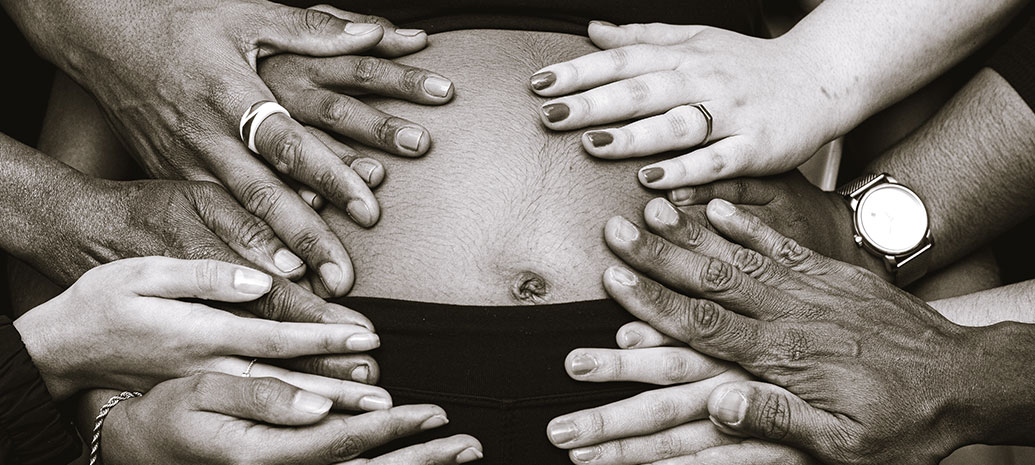 Black & White photo of lots of hands touching a pregnant belly