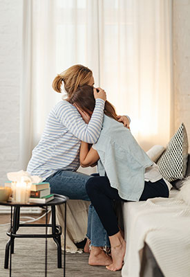 Dark haired woman crying into the shoulder of a light haired woman